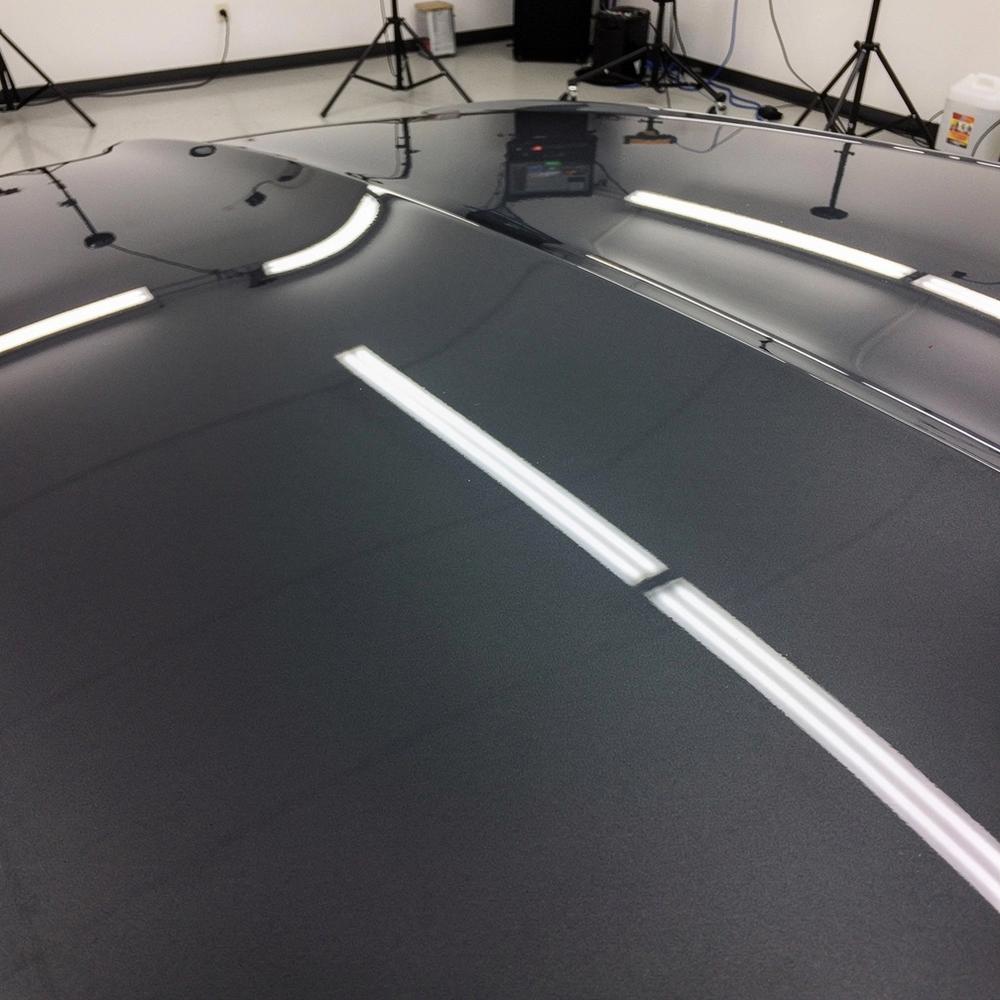The same hood panel after correction and ceramic coating, holding a sharp studio light reflection