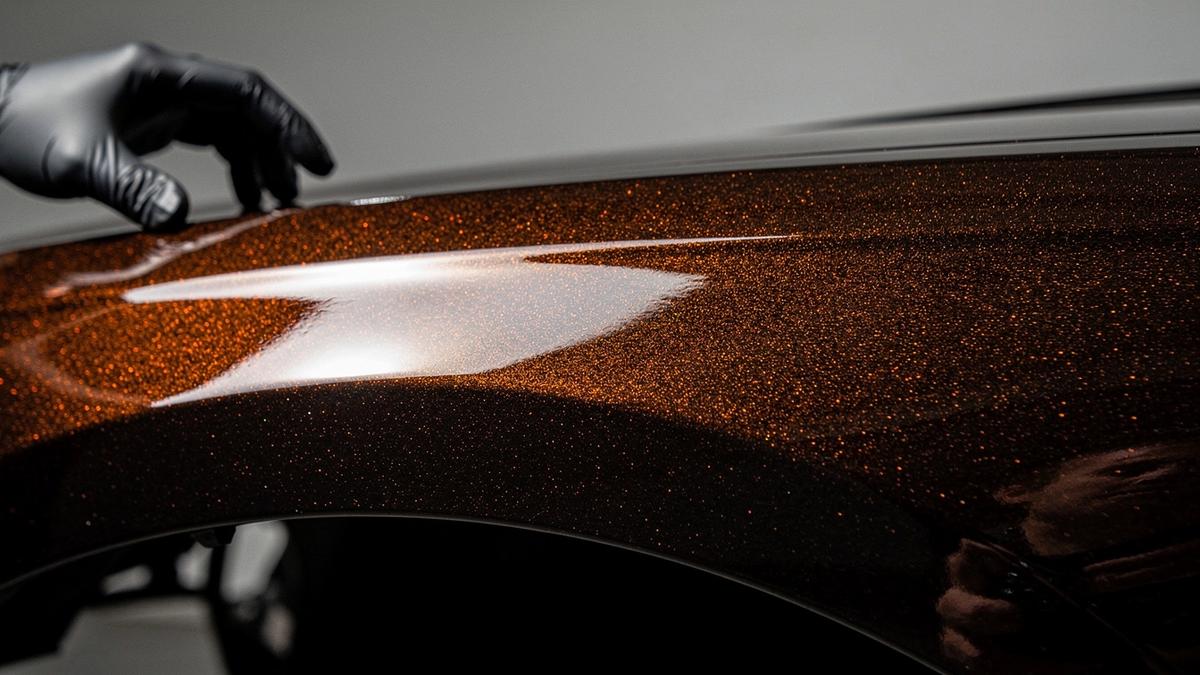 Macro detail of a ceramic coating layer on a dark painted panel edge under raking studio light